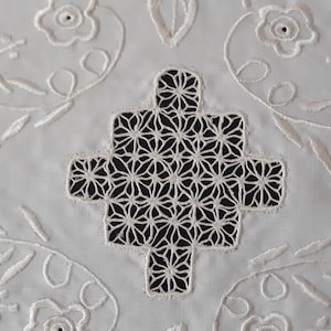 Puede incluir: Mantel de mesa de algodón blanco con bordados intrincados. El centro presenta un gran diseño calado con un patrón geométrico. Los bordes están decorados con motivos florales.
