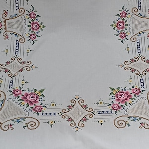 May include: White tablecloth with embroidered floral and basket designs. The embroidery features pink roses, green leaves, and accents of blue, brown, and yellow. The design is symmetrical, with floral arrangements in each corner and along the edges.