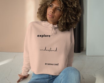 May include: A pink cropped hoodie with the words "explore", "understand", and "transcend" printed on it.