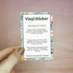 May include: A rectangular vinyl sticker with floral border and the text "Vinyl Sticker" and instructions for use. The sticker is held by a hand with a glittery nail. The background is a light wood surface.