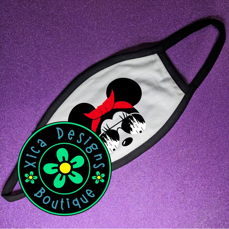 May include: White face mask with a black border. The mask features a black and white illustration of a cartoon mouse wearing sunglasses and a red bow. The text "Xica Designs Boutique" is printed in a circle on the mask.