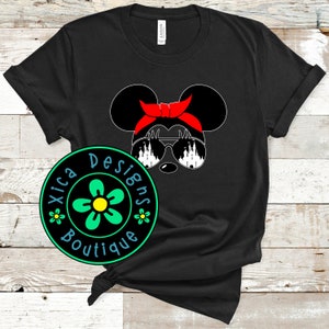 May include: Black t-shirt with a white silhouette of Mickey Mouse wearing sunglasses with a castle design. The sunglasses are reflected in the castle design. Mickey Mouse is wearing a red headband. The shirt has a green circle with a yellow flower and the text "Xica Designs Boutique" in white.