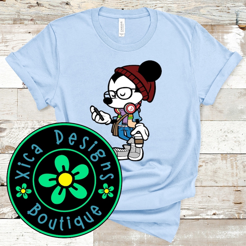 May include: Light blue t-shirt with a cartoon illustration of Mickey Mouse wearing a red beanie, glasses, and headphones. The illustration is in a trendy style and includes a flower design with the text "Xica Designs Boutique".