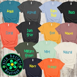Pode incluir: Uma cole&ccedil;&atilde;o de camisetas de v&aacute;rias cores, cada uma exibindo um nome de cor diferente em uma fonte contrastante. As cores incluem Aqua, Asphalt, Baby Blue, Black, Coral, Dark Gray, Gold, Mauve, Military Green, Mint, Natural, Navy e Orange. O logotipo da Xica Designs Boutique &eacute; vis&iacute;vel.