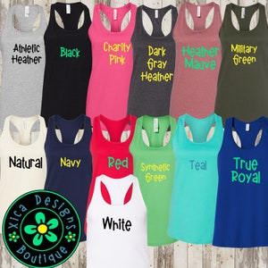 May include: A collection of 11 racerback tank tops in various colors, including athletic heather, black, charity pink, dark gray heather, heather mauve, military green, natural, navy, red, synthetic green, teal, true royal, and white. The tank tops are displayed on a wooden surface.
