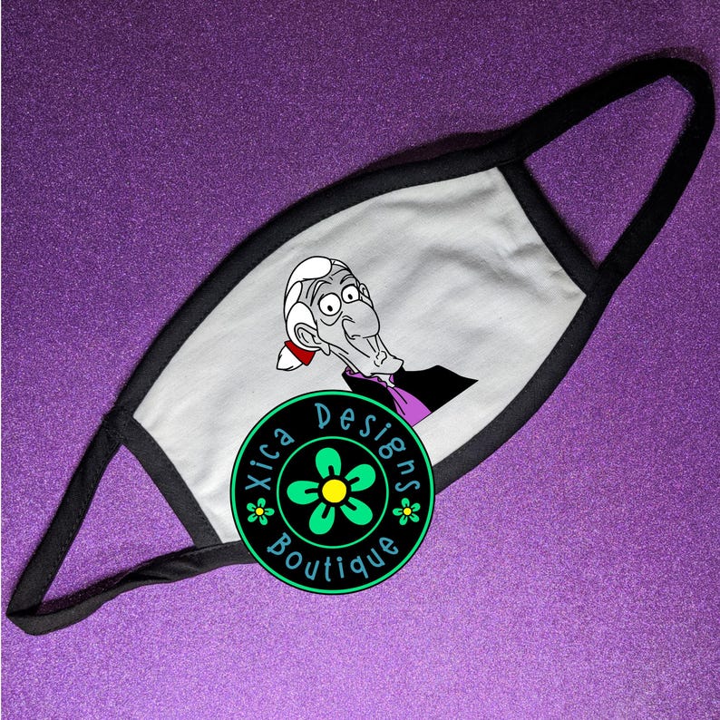 May include: A white face mask with a black border. The mask features a cartoon image of a character with grey hair and a purple shirt. The text "Xica Designs Boutique" is printed on a green circle with a yellow flower.