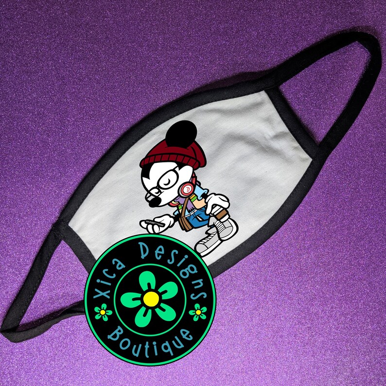 May include: White face mask with a black border. The mask features a cartoon illustration of Mickey Mouse wearing a red beanie, glasses, and headphones. The text "Xica Designs Boutique" is printed in a circle below the illustration.