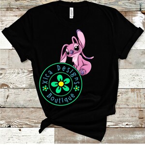Puede incluir: Camiseta negra con un personaje de dibujos animados rosa con orejas grandes y una expresi&oacute;n amigable. La camiseta incluye un logotipo circular verde y amarillo con el texto "Xica Designs Boutique".