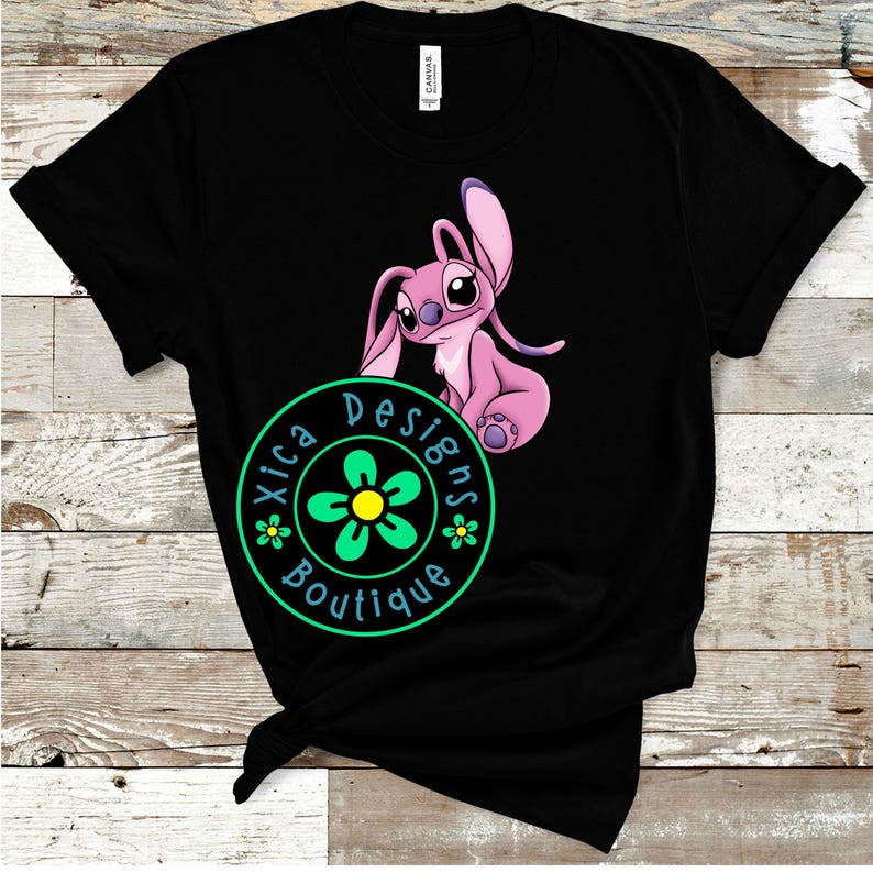 Puede incluir: Camiseta negra con un personaje de dibujos animados rosa con orejas grandes y una expresi&oacute;n amigable. La camiseta incluye un logotipo circular verde y amarillo con el texto "Xica Designs Boutique".