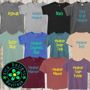 K&ouml;nnte beinhalten: Eine Sammlung von zehn T-Shirts in verschiedenen Farben und Melange-Farbt&ouml;nen. Jedes Shirt hat eine andere Farbe und einen anderen Text, darunter "Asphalt", "Athletic Heather", "Schwarz", "Dunkelgrau Melange", "Staubiges Blau", "Heather Columbia Blau", "Heather Tief T&uuml;rkis", "Heather Staub", "Heather Maroon", "Heather Mauve", "Heather Team Lila".