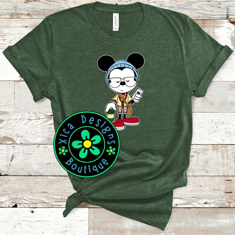May include: Green t-shirt with a cartoon image of Mickey Mouse wearing glasses and holding a phone. The image is surrounded by a black circle with the text "Xica Designs Boutique" in green and white.