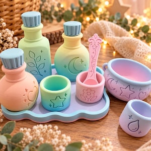 May include: A set of pastel-coloured potion bottles, small cups, a cauldron, and a spoon on a wavy tray. The items feature embossed designs including a leaf, moon, heart, star, flower, and raindrop. The pieces are light blue, green, yellow, and pink.