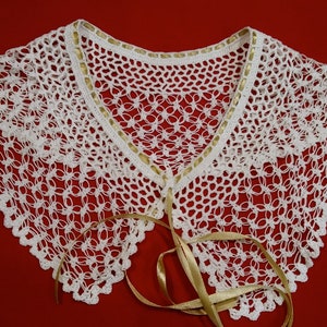 Puede incluir: Collar blanco de ganchillo con un lazo de cinta dorada. El collar está hecho de encaje delicado y tiene un borde festoneado.