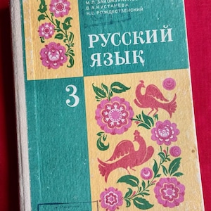 Pode incluir: Um livro didático de capa dura intitulado "РУССКИЙ ЯЗЫК" com o número 3 na capa. O design apresenta blocos alternados verdes e amarelos com padrões florais rosa e duas ilustrações de pássaros vermelhos. Os autores são M. L. Zakozhnikova, V. A. Kustareva e N. S. Rozhdestvensky.