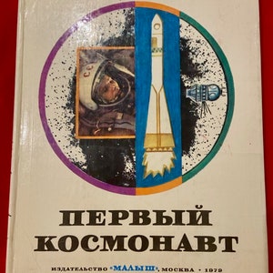 Puede incluir: Una portada de libro vintage con una ilustración colorida de un cohete, una cápsula espacial y un cosmonauta. El título del libro es "ПЕРВЫЙ КОСМОНАВТ" y el autor es "Виктор Синицин". El libro fue publicado por "МАЛЫШ" en Moscú en 1979.