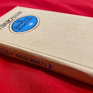 May include: A beige book with the title "СПРАВОЧНИК по французской косметике" in black text. The book has a blue circle with white text on the front cover.