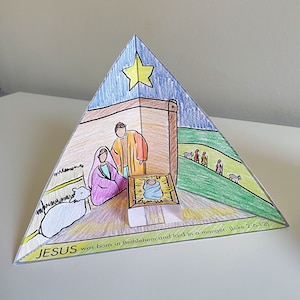 May include: A paper craft depicting the nativity scene with a yellow star, a blue sky, a brown manger, a baby Jesus, Mary, Joseph, and sheep. The text reads "JESUS was born in Bethlehem and laid in a manger. (Luke 2:6-12)"