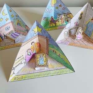Puede incluir: Un conjunto de cuatro pirámides de papel de colores con ilustraciones que representan la historia del nacimiento de Jesús. Cada pirámide tiene una escena diferente: María y José viajando, María rezando, el nacimiento de Jesús y una estrella en el cielo. El texto en las pirámides dice: "PH heard God's plan through a", "Y & JOSEPH", "MARY had an obedient heart to God's plan", y "JESUS was born in Bethlehem and laid in a manger. (Luke 2:6-12)"