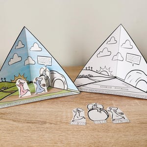 Może przedstawiać: Drukowana, wielkanocna zabawka dla dzieci z dioramą pustego grobu, do którego biegną trzy kobiety. Diorama jest wykonane z papieru i można je pokolorować. Zabawka zawiera również trzy oddzielne papierowe figurki kobiet, które biegną.