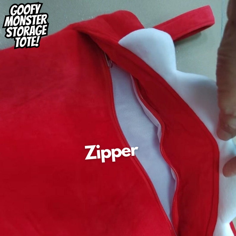 May include: Red tote bag with a white zipper and the words "GOOFY MONSTER STORAGE TOTE!" printed on the front. The zipper is open and the inside of the bag is white.