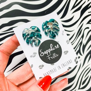 May include: A pair of teal green and silver monstera leaf earrings. The earrings are handmade in England by Sapphire Frills.