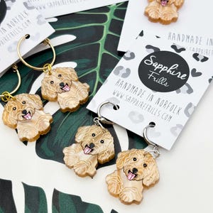 May include: Earrings featuring a light brown dog design with a smiling expression. The earrings are attached to gold and silver hoops. The earrings are displayed on white cards with the text "Sapphire Frills" and "Handmade in Norfolk".