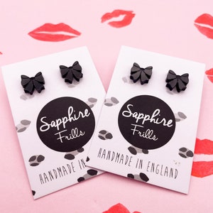 May include: A pair of black bow earrings on a white card with the text "Sapphire Frills" and "Handmade in England".