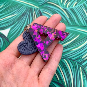 May include: A pink and black glitter resin letter A keychain with a black heart charm.
