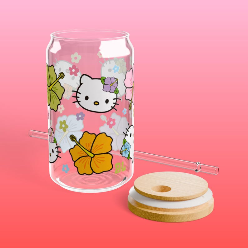 May include: A clear glass can with a pink background and a design of Hello Kitty and hibiscus flowers. The can has a bamboo lid and a glass straw.