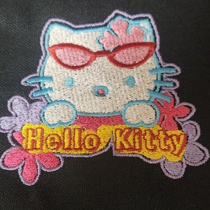 May include: Embroidered patch featuring Hello Kitty wearing sunglasses and a flower on her head. The patch is surrounded by purple, pink, and yellow flowers. The text "Hello Kitty" is embroidered in yellow.