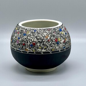 May include: A white ceramic bowl with a black rim and base. The bowl is decorated with a black and white pattern and colorful dots.