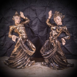 May include: A pair of ceramic figurines of dancers in gold and black. The figurines are posed in a dynamic dance position.