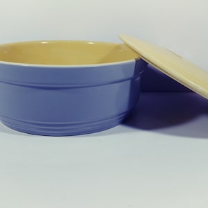 May include: A blue ceramic bowl with a yellow interior and a matching yellow lid. The bowl has a rounded shape and a slightly flared rim.