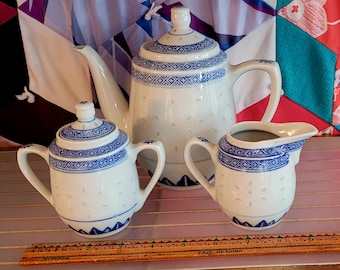May include: A white teapot, sugar bowl, and creamer set with blue and white floral designs. The set is made of porcelain and has a traditional Chinese style.