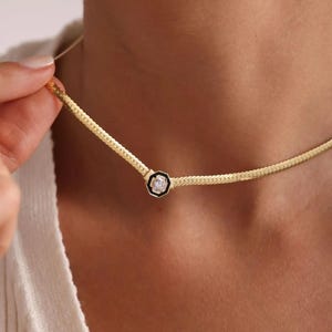 Puede incluir: Un collar de cadena de oro con un pequeño colgante octogonal con una piedra preciosa transparente engastada en un marco de esmalte negro.