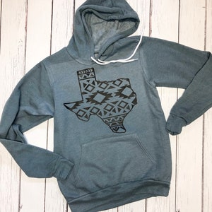 May include: A teal blue hooded sweatshirt with a black outline of the state of Texas, filled with a geometric pattern.