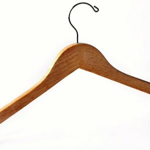 Puede incluir: Una percha de madera con un acabado natural y un gancho de metal. La percha tiene una forma curva y est&aacute; dise&ntilde;ada para sostener la ropa sin causar arrugas.