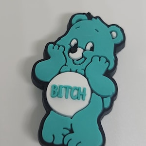 May include: A teal bear-shaped charm with a black outline. The bear is holding its paws up to its face. A white circle on the bear's belly has the word "BITCH" in teal letters.