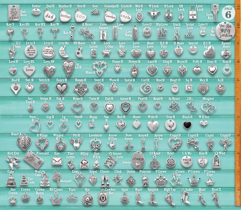 Puede incluir: Una colecci&oacute;n de dijes de metal plateado en varias formas, incluyendo corazones, llaves, coronas y letras, dispuestos en filas sobre un fondo verde azulado con una regla vertical en el lado derecho que muestra medidas en cent&iacute;metros.