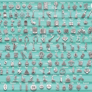 May include: A collection of silver-toned metal charms arranged in a grid on a light blue background, featuring various shapes like musical instruments, sports equipment, and tools. A wooden ruler on the right shows a scale of 10 inches.