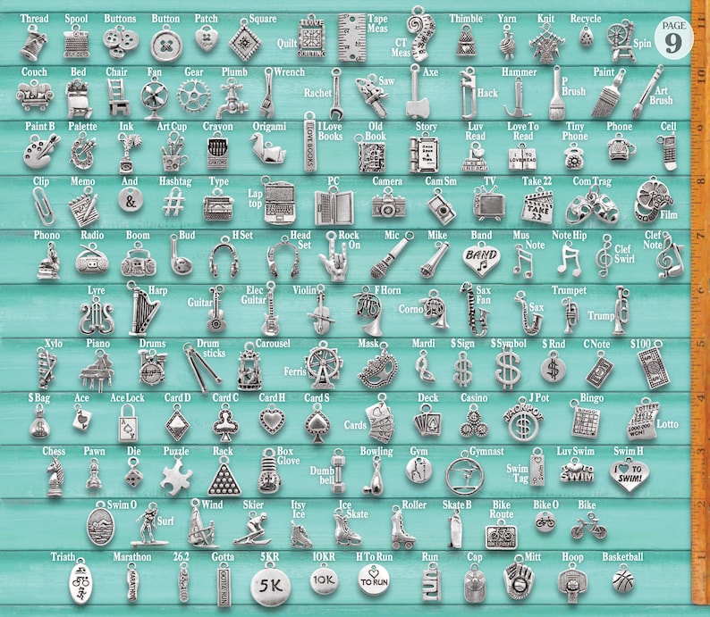 May include: A collection of silver-toned metal charms arranged in a grid on a light blue background, featuring various shapes like musical instruments, sports equipment, and tools. A wooden ruler on the right shows a scale of 10 inches.