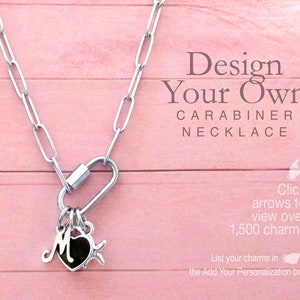 May include: A silver-toned paperclip chain necklace featuring a carabiner clasp. Three charms are attached to the carabiner: a silver letter M, a black heart, and a silver star. Text reads: Design Your Own CARABINER NECKLACE. Click arrows to view over 1,500 charms. List your charms in the Add Your Personalization box.