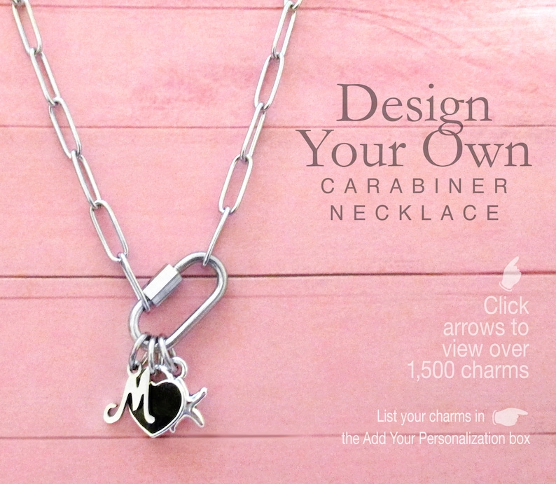 May include: A silver-toned paperclip chain necklace featuring a carabiner clasp. Three charms are attached to the carabiner: a silver letter M, a black heart, and a silver star. Text reads: Design Your Own CARABINER NECKLACE. Click arrows to view over 1,500 charms. List your charms in the Add Your Personalization box.