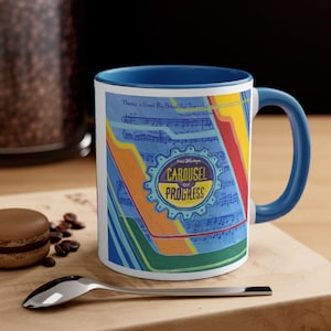 May include: A blue and white ceramic mug with a colorful design featuring a gear with the text "Walt Disney's Carousel of Progress" and musical notes. There's a great big beautiful tomorrow.