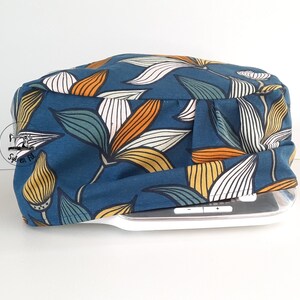 Peut inclure: Une housse en tissu bleu avec un motif floral dans les tons orange, jaune, blanc et vert. La housse est conçue pour s'adapter à une machine à coudre.