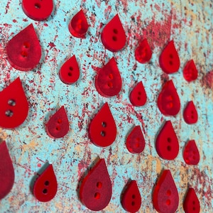 May include: A collection of red teardrop-shaped buttons with two holes each. The buttons are arranged in a pattern on a textured blue and orange background.