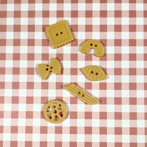 Peut inclure: Un ensemble de six boutons en forme de pâtes brunes. Les boutons sont en forme de nœud papillon, de roue, de longue nouille, de feuille, de carré et de fer à cheval.