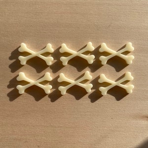 May include: Six pairs of white bone-shaped charms, arranged in two rows of three. Each charm is shaped like two crossed bones.