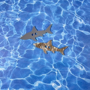 May include: Two grey shark-shaped buttons on a blue background with a water ripple pattern.