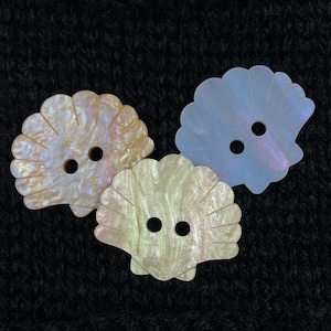 May include: Three iridescent shell-shaped buttons with two holes each. The buttons are in shades of white, beige, and light purple.